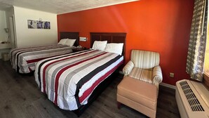 Una habitación de hotel con dos camas, un sillón a rayas y un pequeño reposapiés.