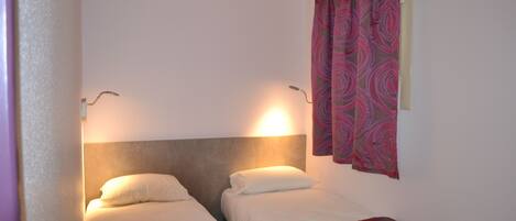 A small, well-lit room with two single beds, each with a headboard and a bedside lamp.