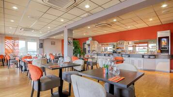 A modern restaurant with multiple dining tables and chairs, a kitchen area, and a bright interior.