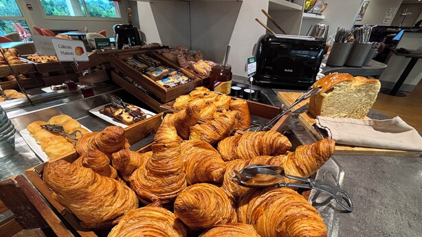 Una vitrina de panadería con diversas opciones de repostería, incluyendo croissants y pan, dispuestas en cajas y bandejas de madera.