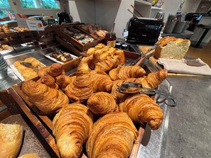 A bakery display with various baked goods, including croissants and bread, arranged in wooden boxes and trays. - Brit Hotel Les Evens (Saint-Saturnin)