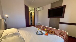 Una habitación de hotel con una cama, un televisor montado en la pared y una bandeja de desayuno sobre la cama.