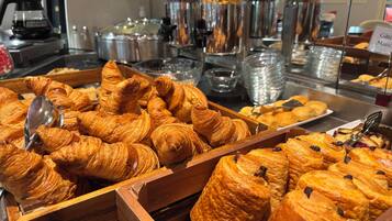 Un bufé con diversas opciones de panadería, incluyendo croissants y pasteles, dispuestas en bandejas de madera.