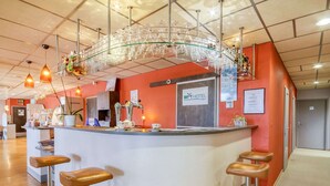 Zona de recepción de hotel con una barra de vidrio curva, dos taburetes, un letrero que dice "BRIT HOTEL Comfort" y una escalera que sube a otro piso.
