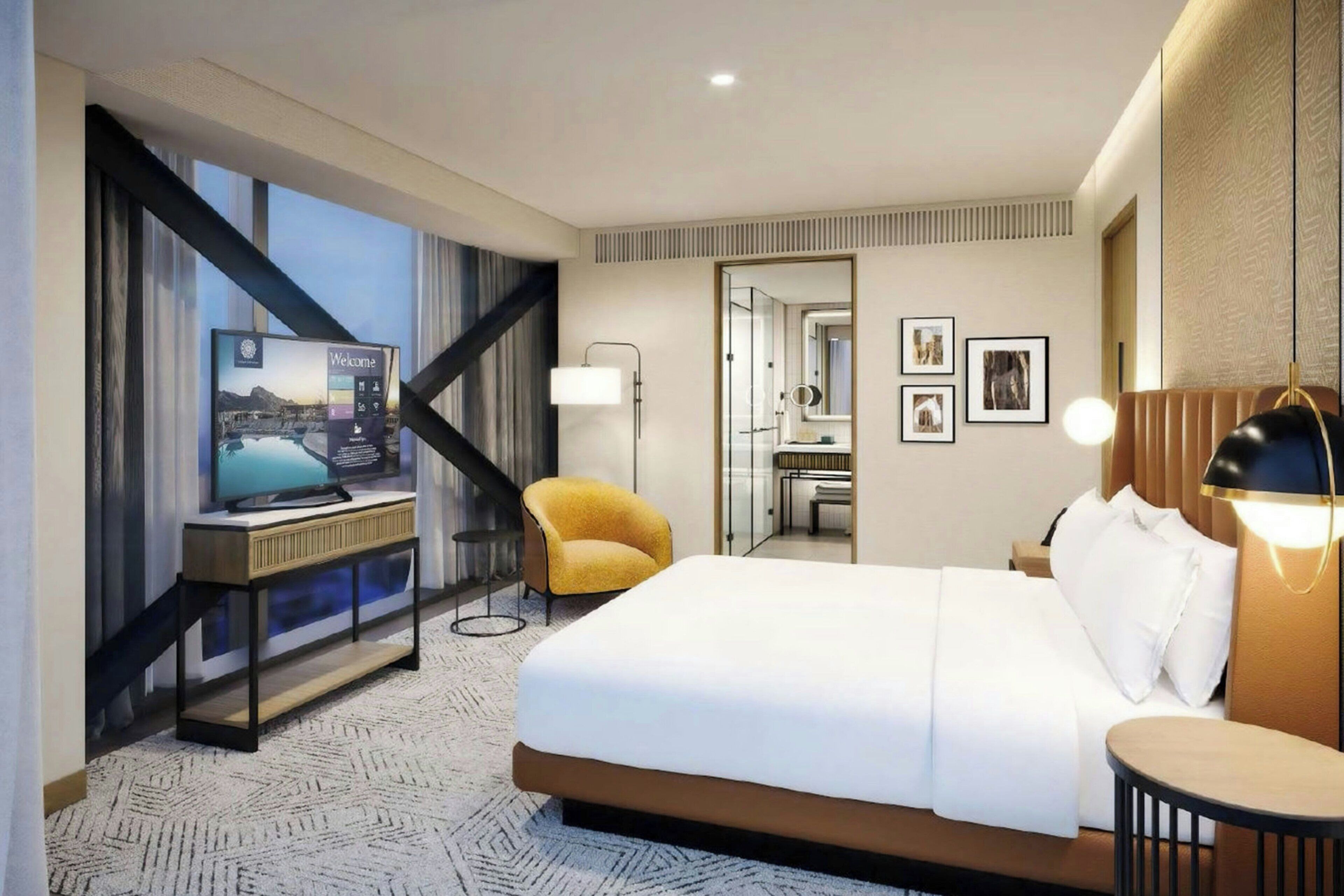 Una habitación de hotel moderna con una cama grande, un escritorio con computadora, una silla, una mesita de noche y un espejo.