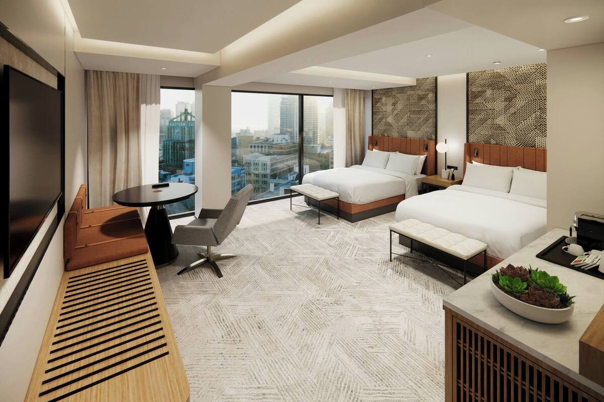 A modern hotel room with a large bed, a smaller bed, a desk, a TV, and a view of the city.