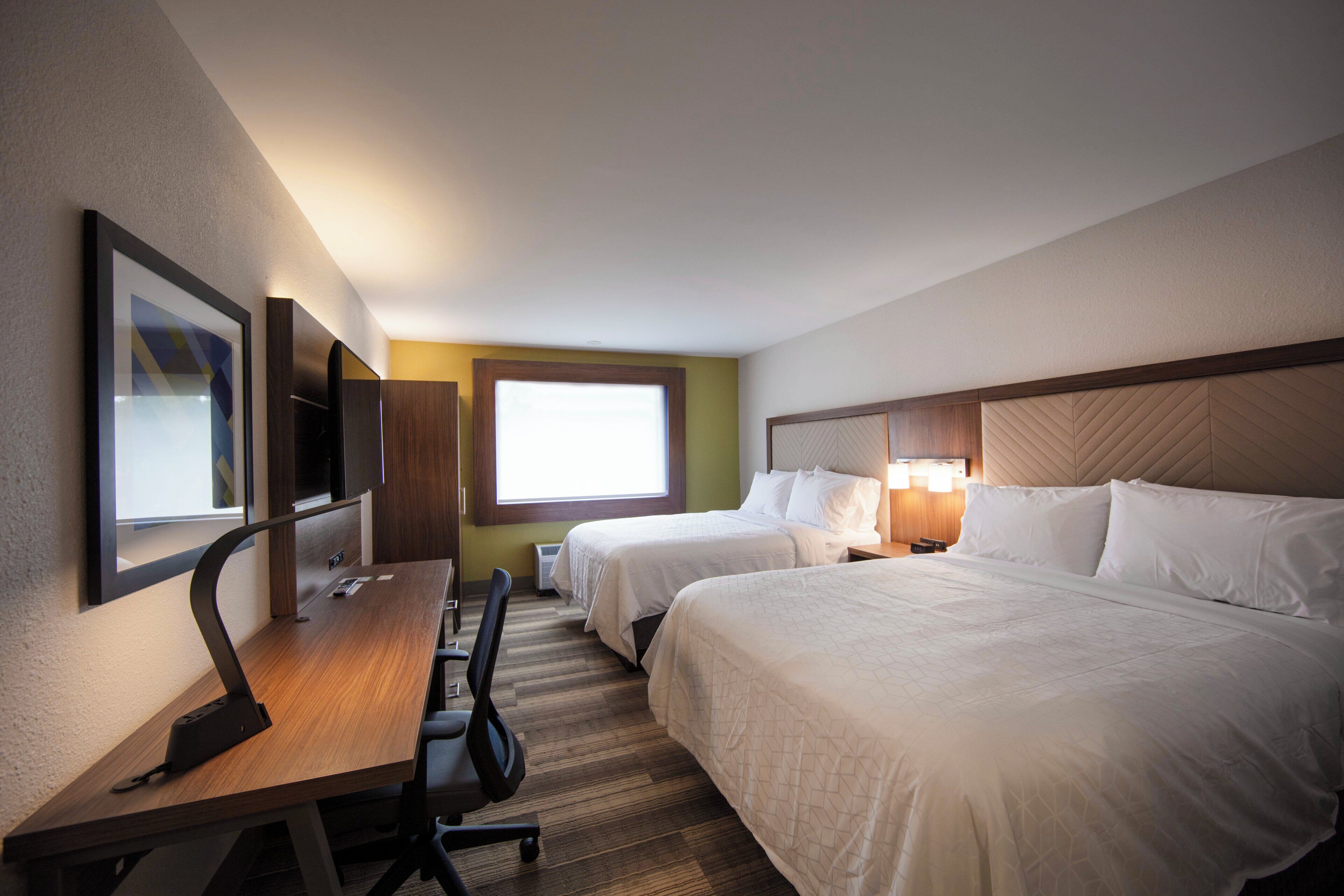 A hotel room with two beds, a desk, a chair, a TV, and a window.
