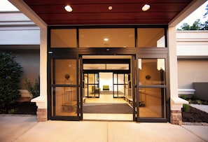 A hotel entrance with a glass door, a reception desk, and a green chair visible inside.