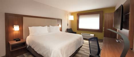 A hotel room with a large bed, bedside tables, a desk with a chair, a television, and a window with blinds.