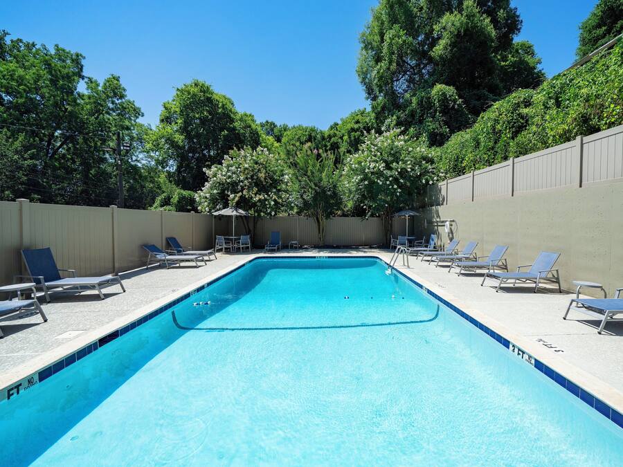 Una piscina rectangular con una marca de profundidad de 3 pies, rodeada de sillas de descanso y una cerca, con árboles al fondo.