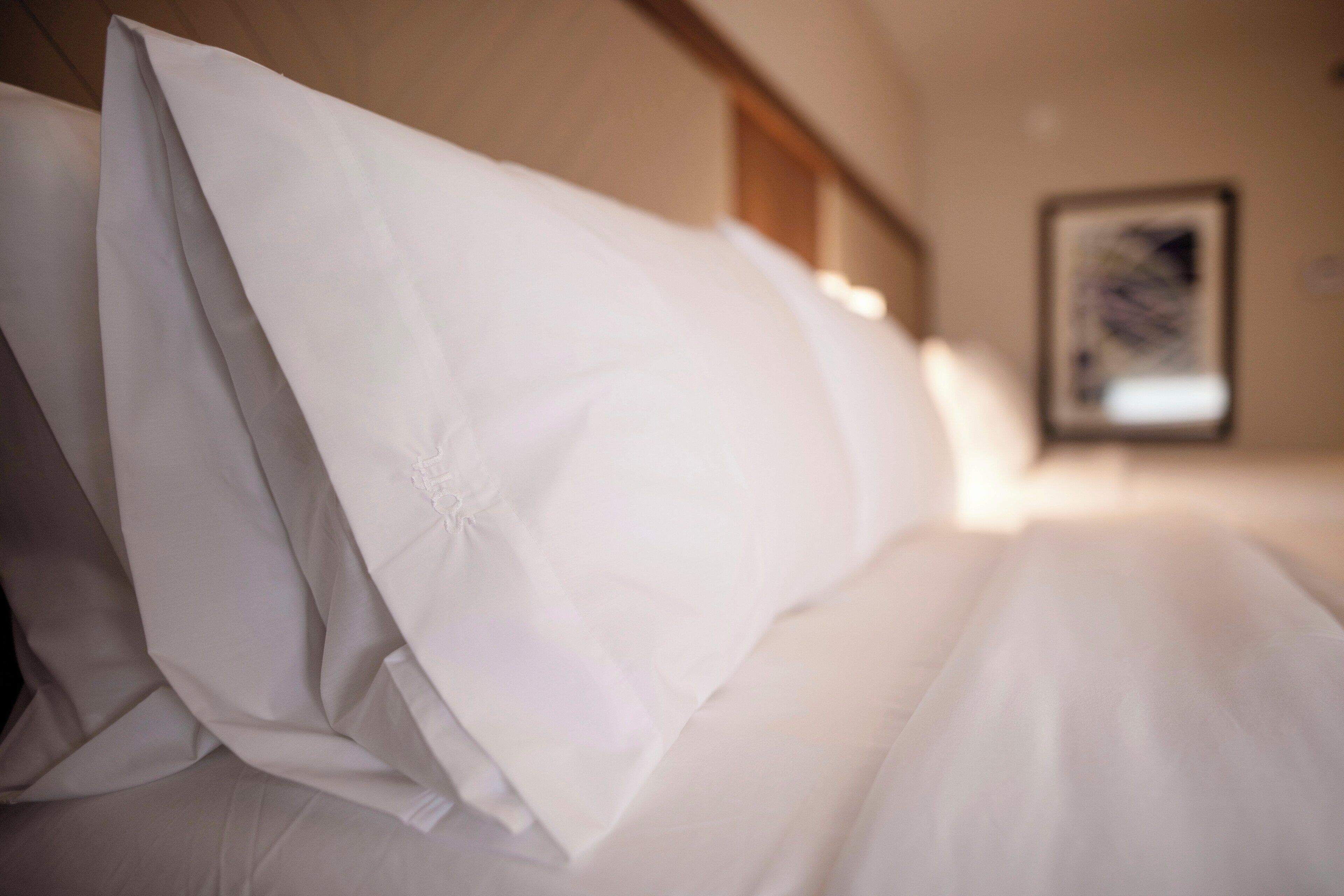 A hotel room with a neatly made bed, a framed picture on the wall, and a wooden headboard.