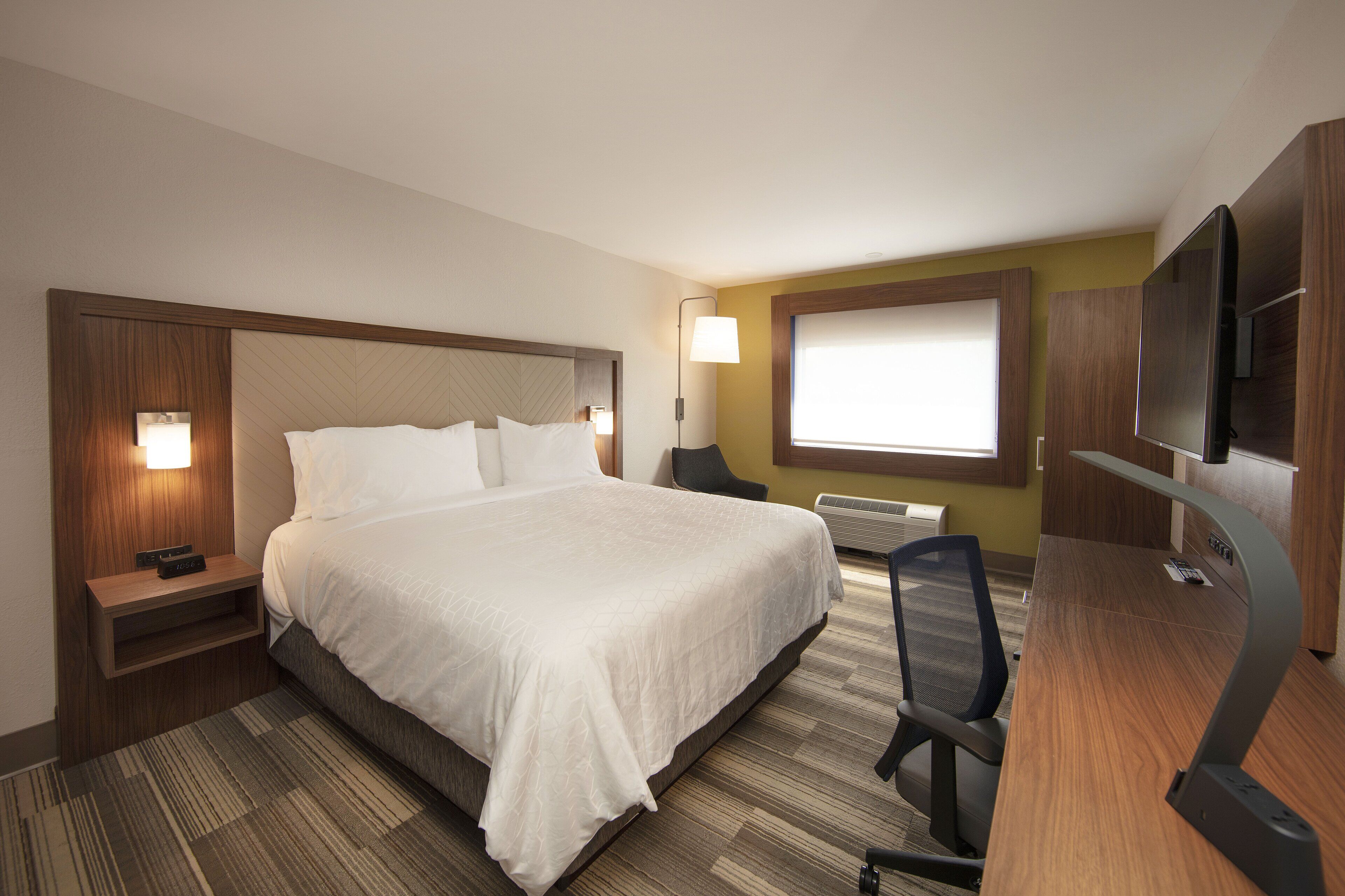 A hotel room with a large bed, a desk with a chair, a TV, and a window with blinds.