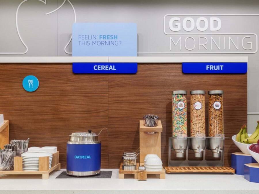A breakfast bar with labeled sections for cereal and fruit, a blue oatmeal container, and condiments.