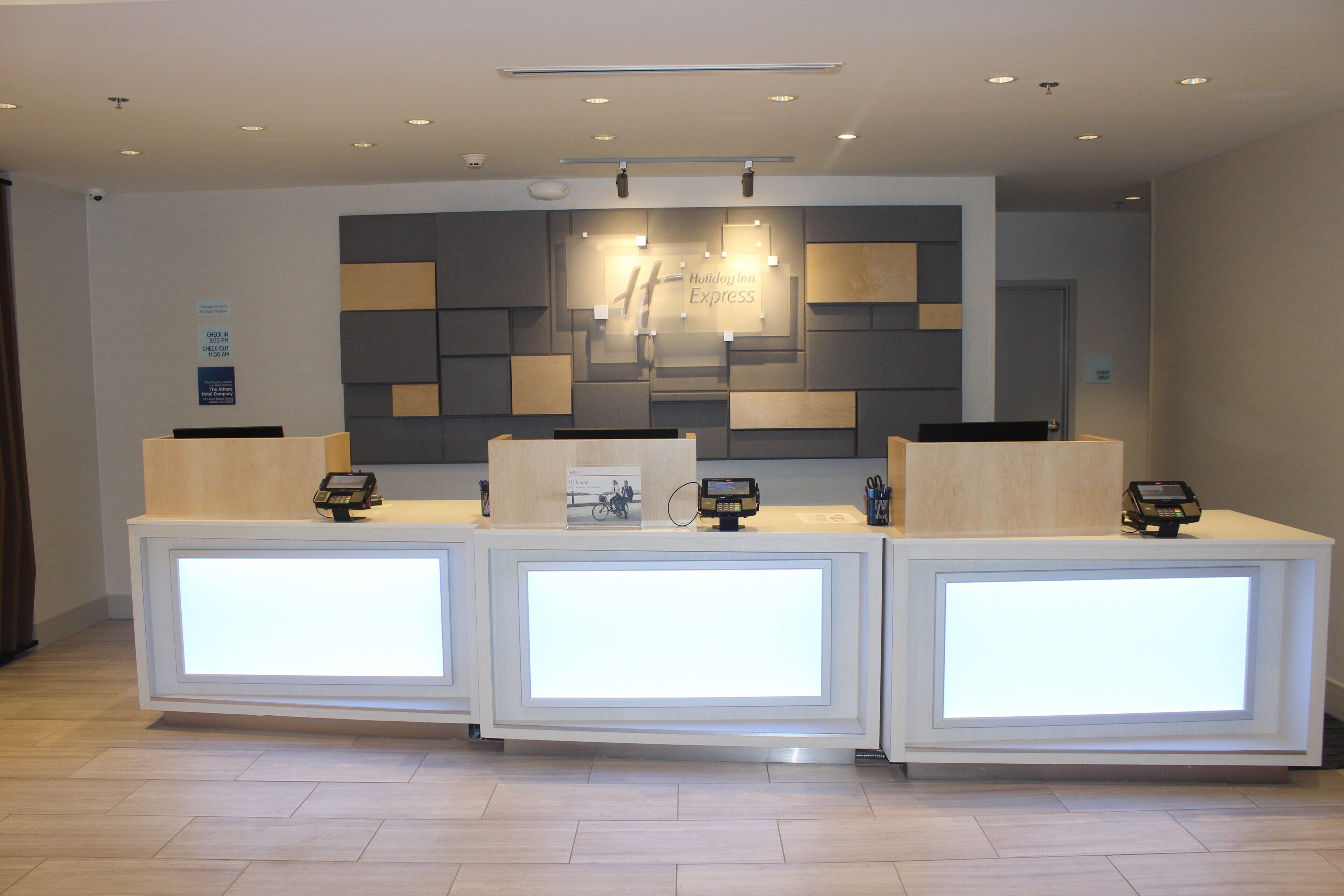 A reception desk area with three counters, a wall-mounted sign for Holiday Inn Express, and a security camera on the ceiling.