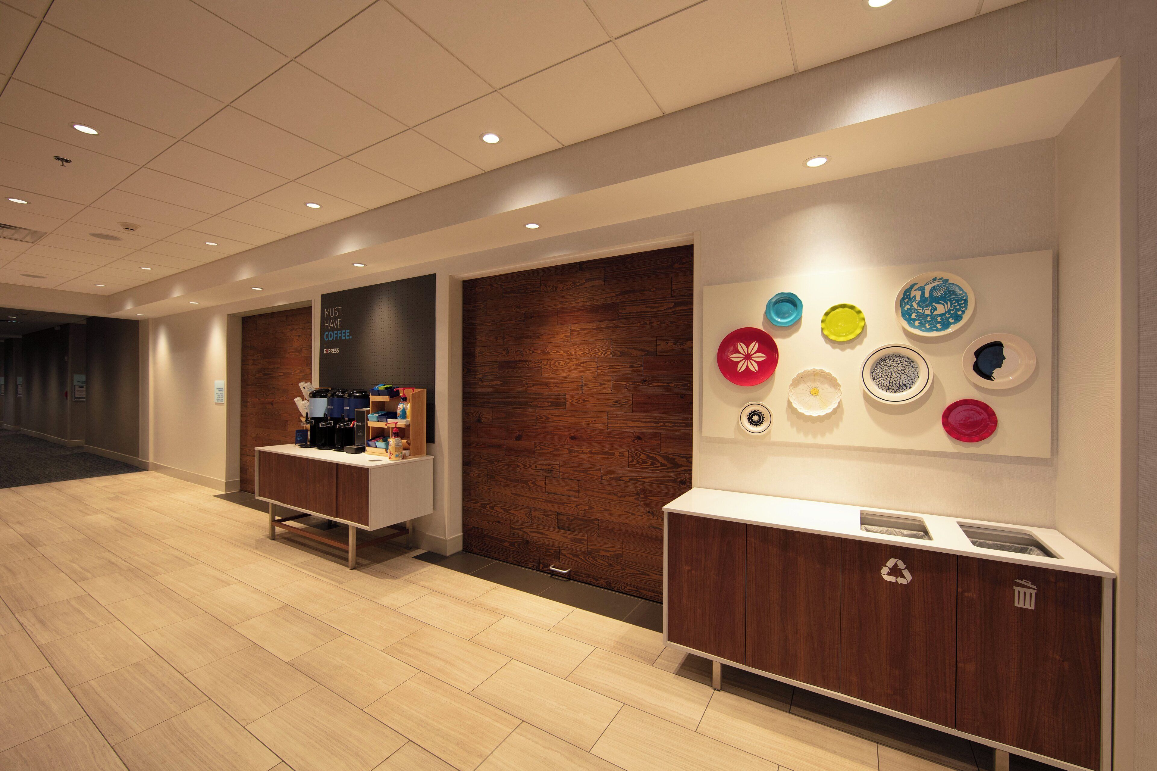 Un hall d’hôtel comprenant un coin café, une poubelle de recyclage et un mur décoré d’assiettes.