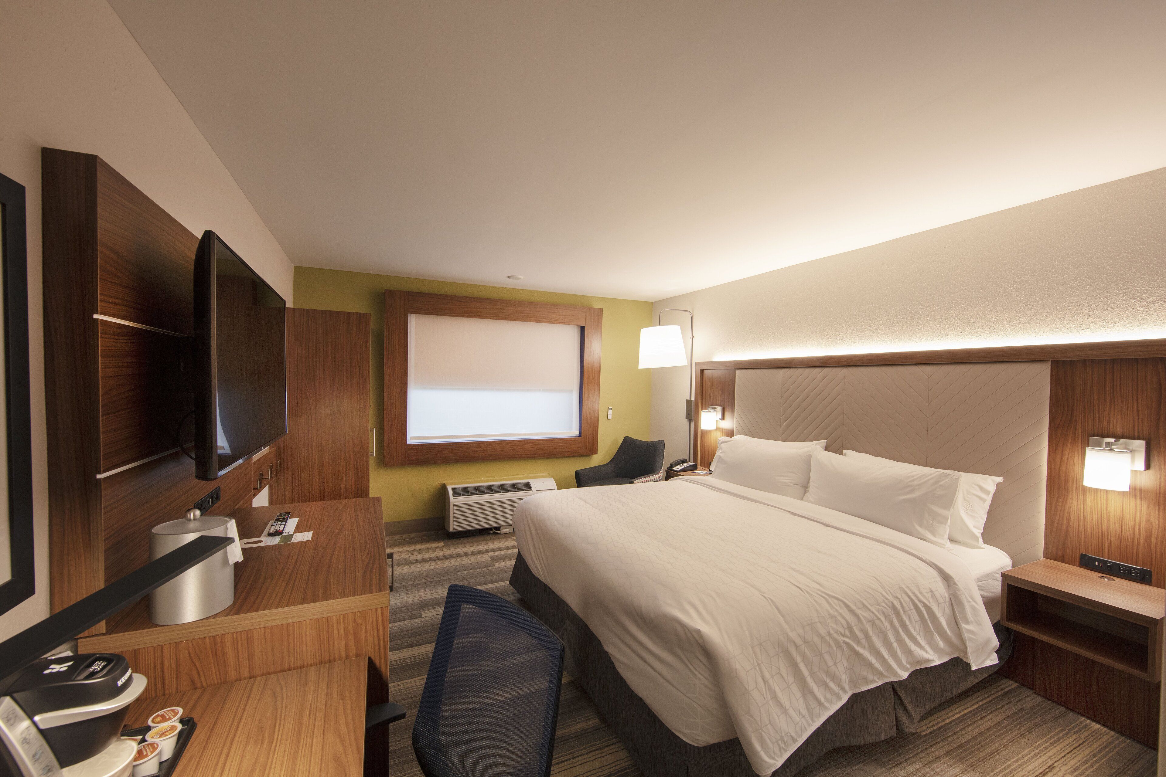 A hotel room with a large bed, a desk with a coffee maker, a TV, and a window with a view.