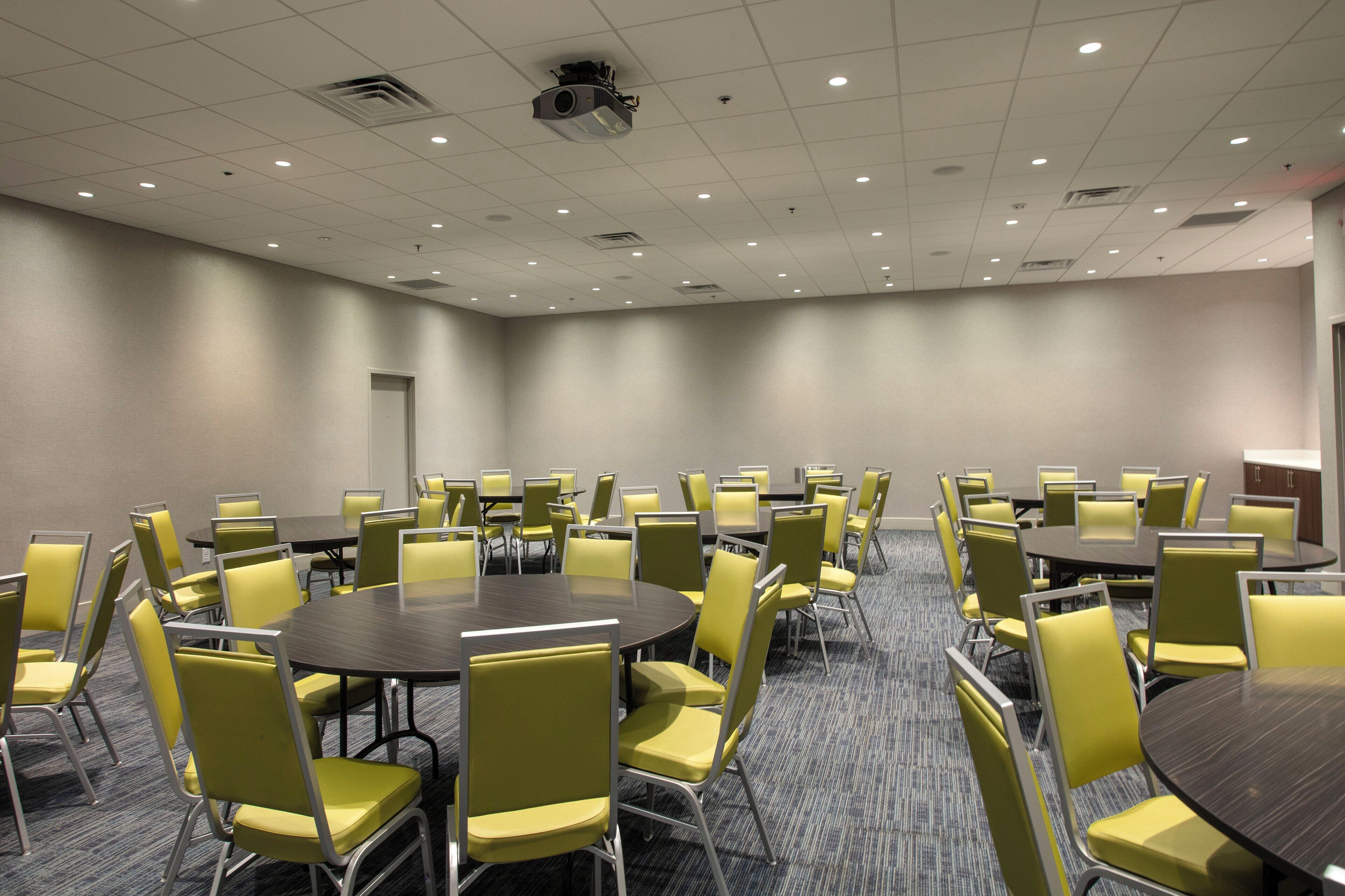 A conference room with multiple tables and chairs, equipped with a ceiling projector.
