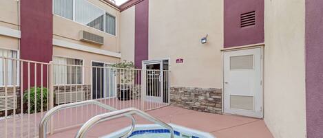 A swimming pool with a metal ladder, surrounded by a stone wall and a beige building with purple accents.
