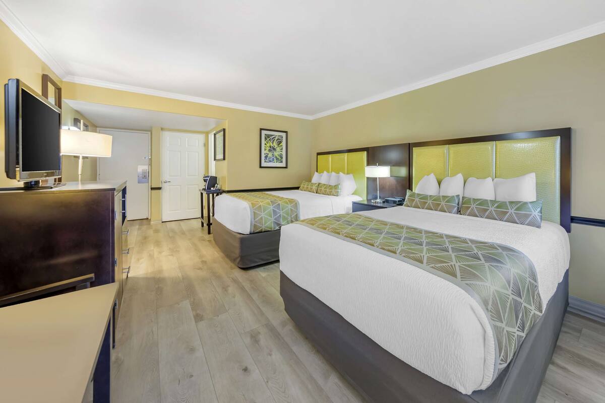 A hotel room with two beds, a desk, a television, and a door.