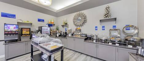 A modern breakfast area with self-service stations, including coffee machines and a variety of food options.