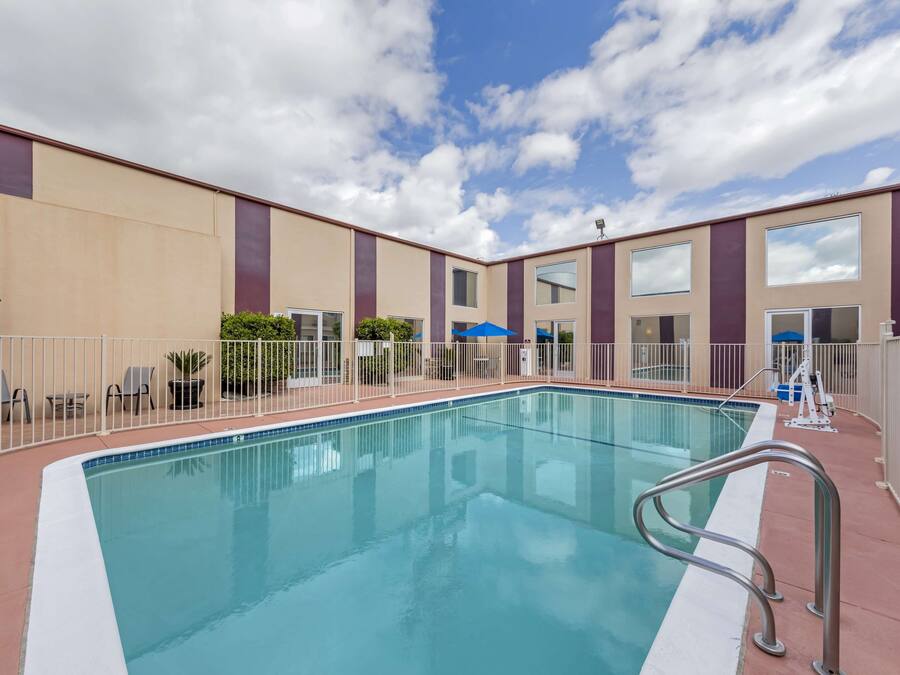 A swimming pool with a white border, surrounded by a fence, and adjacent to a building with large windows and a flat roof.
