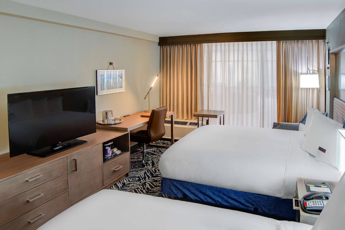 A hotel room with a large bed, a desk with a chair, a television, and a small table.