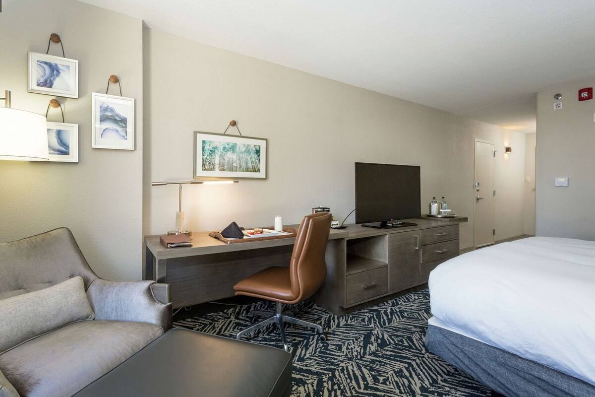 A hotel room with a bed, a desk with a chair, a television, and artwork on the wall.