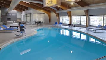 An indoor swimming pool with clear blue water, surrounded by lounge chairs and a modern interior with wooden beams and large windows.