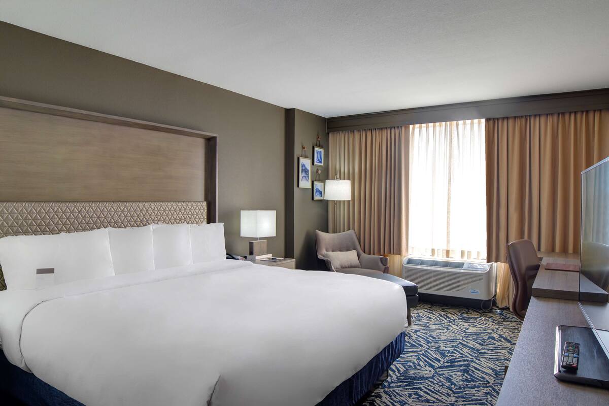 A hotel room with a large bed, a desk with a computer, a chair, a lamp, and a TV.