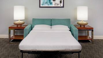 Una cama individual con cabecera color verde azulado, flanqueada por dos mesitas de noche con lámparas, en una habitación con alfombra de diseño geométrico.