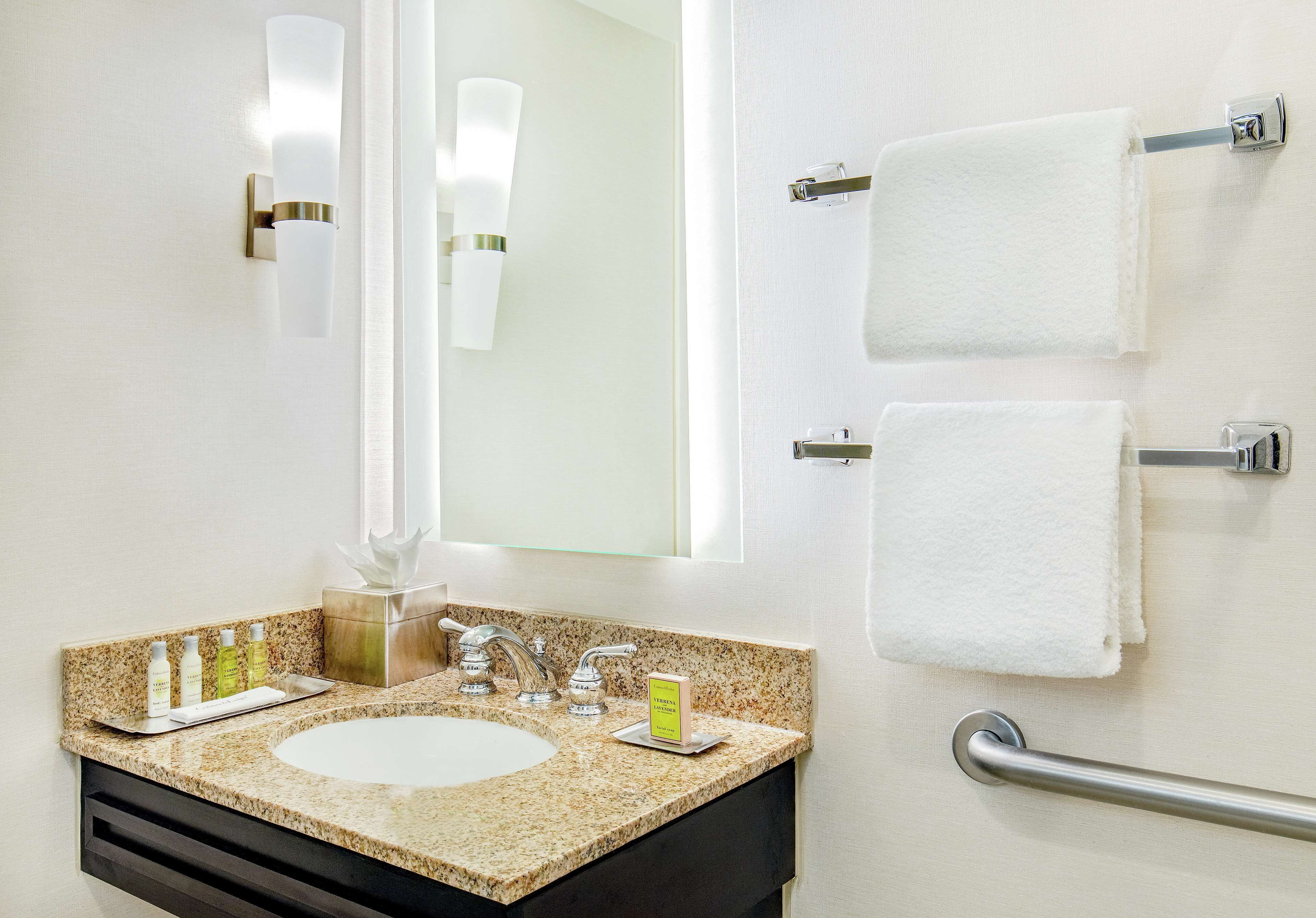 A bathroom with a granite countertop sink, two towel racks, a mirror, and a handrail.