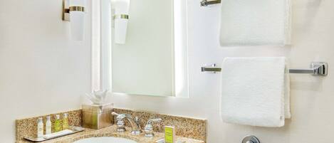 A bathroom with a granite countertop sink, two towel racks, a mirror, and a handrail.