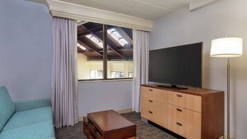 A room with a sofa, a TV on a wooden cabinet, a lamp, and a window with curtains.