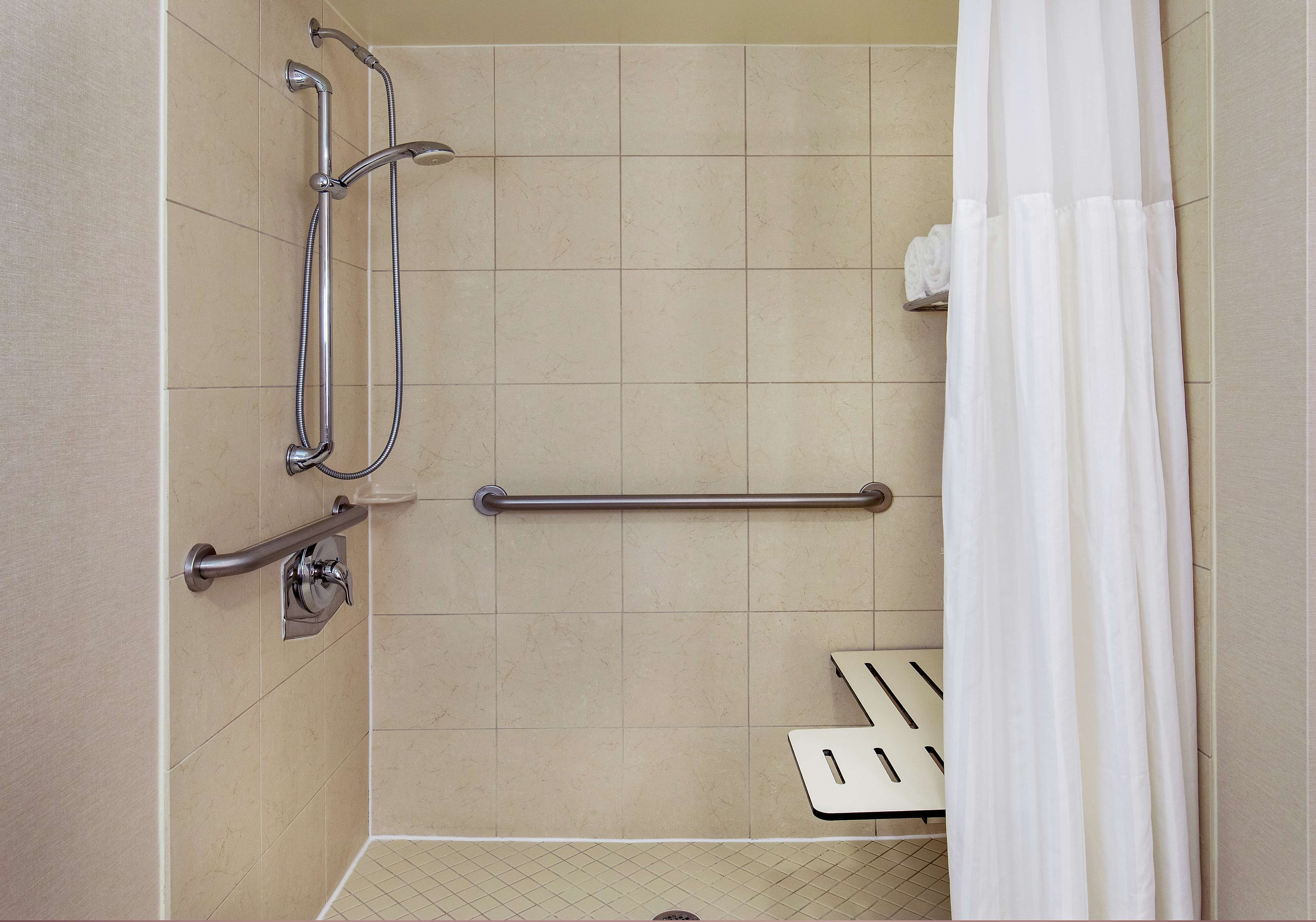 A shower area with a grab bar, a hand-held showerhead, and a white shower curtain.