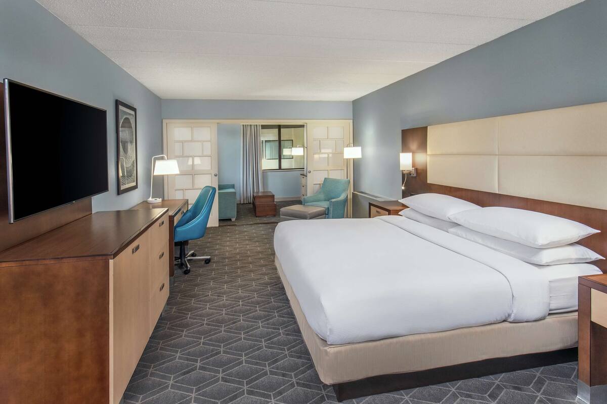 Quarto de hotel com uma cama grande, uma escrivaninha com televisão de tela plana, uma cadeira e uma mesinha.