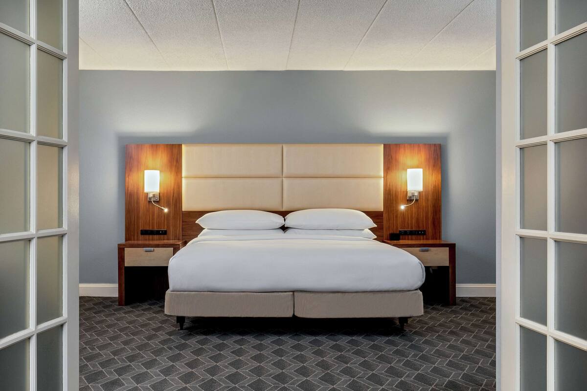 Quarto de hotel com uma cama grande, duas mesas de cabeceira e cabeceira com iluminação embutida.