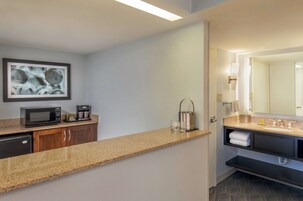 Un baño moderno con un espejo grande, lavamanos y una cafetera sobre la encimera.