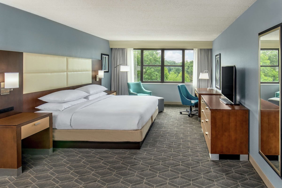 Quarto de hotel com uma cama grande, uma escrivaninha, uma cadeira, um armário e uma televisão.