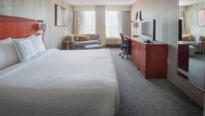 A hotel room with a large bed, a desk with a computer, a chair, and a television.