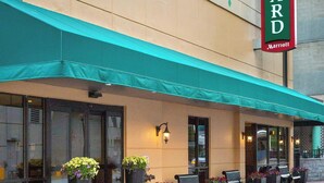 A Courtyard Marriott hotel with a green awning, outdoor seating, and potted plants.