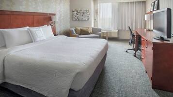 A hotel room with a large bed, a desk with a television, a chair, and a small table.
