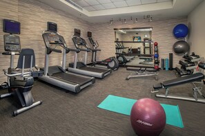 Une salle de sport équipée de tapis de course, de vélos elliptiques, d’un banc de développé couché et de ballons d’exercice.