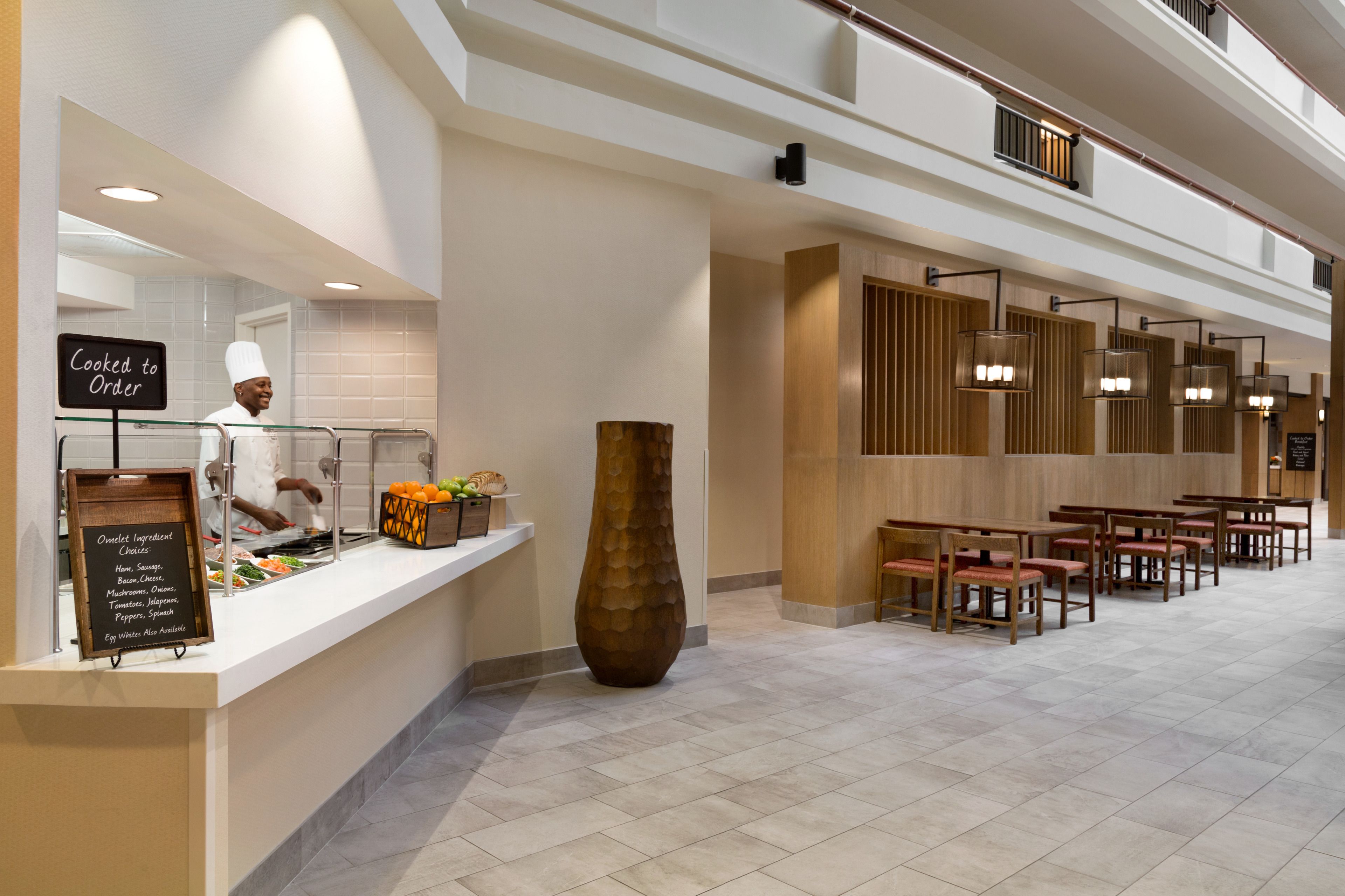 A hotel lobby with a food counter, a chef, a large vase, and seating area.