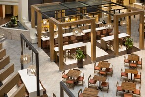 Un vaste espace de restauration intérieur, doté de nombreuses tables et chaises en bois, et entouré de cloisons en verre et de plantes en pot.