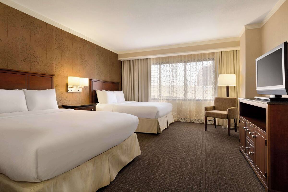 A hotel room with two beds, a TV, a desk, and a chair.