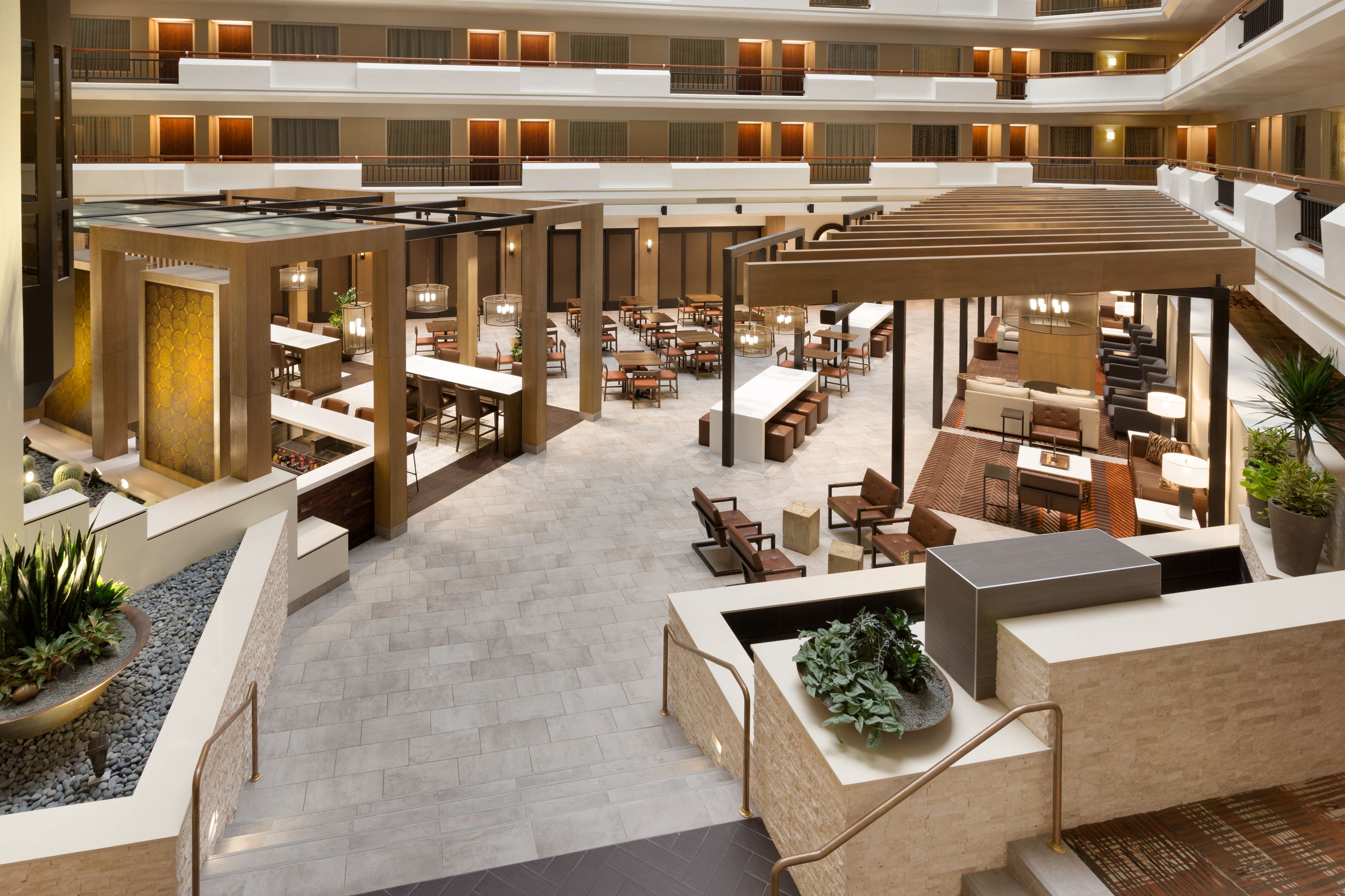 Un amplio vestíbulo de hotel con varias zonas de comedor, un área de estar central y una escalera que conduce a pisos superiores.