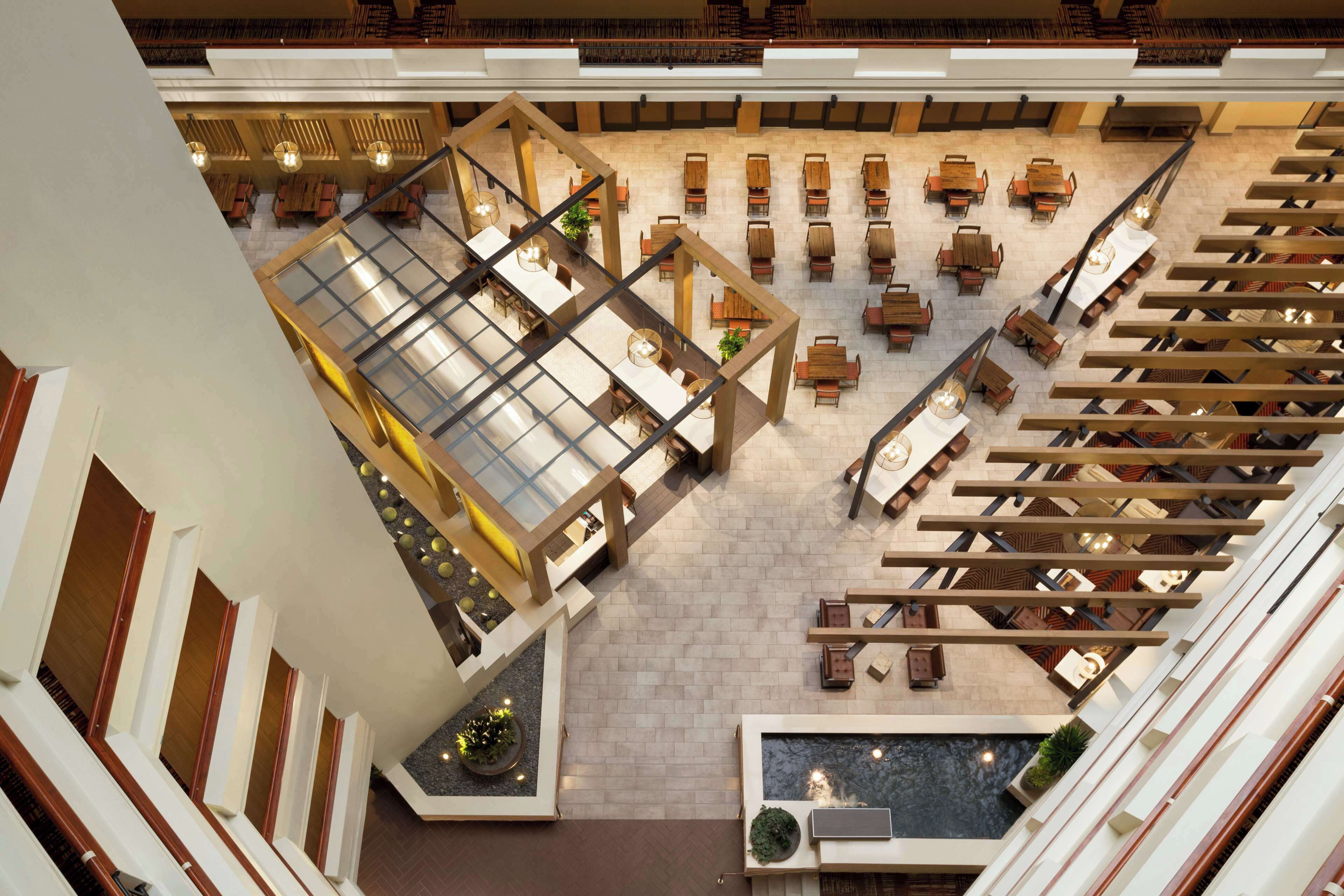 A spacious atrium with multiple seating areas, a central water feature, and a glass ceiling.