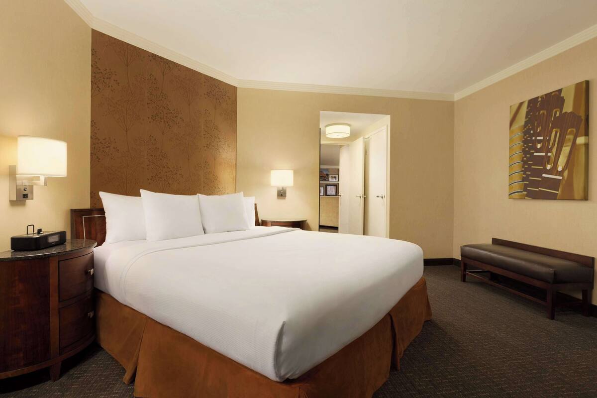 A hotel room with a large bed, bedside tables, a bench, and a wall with a decorative panel.