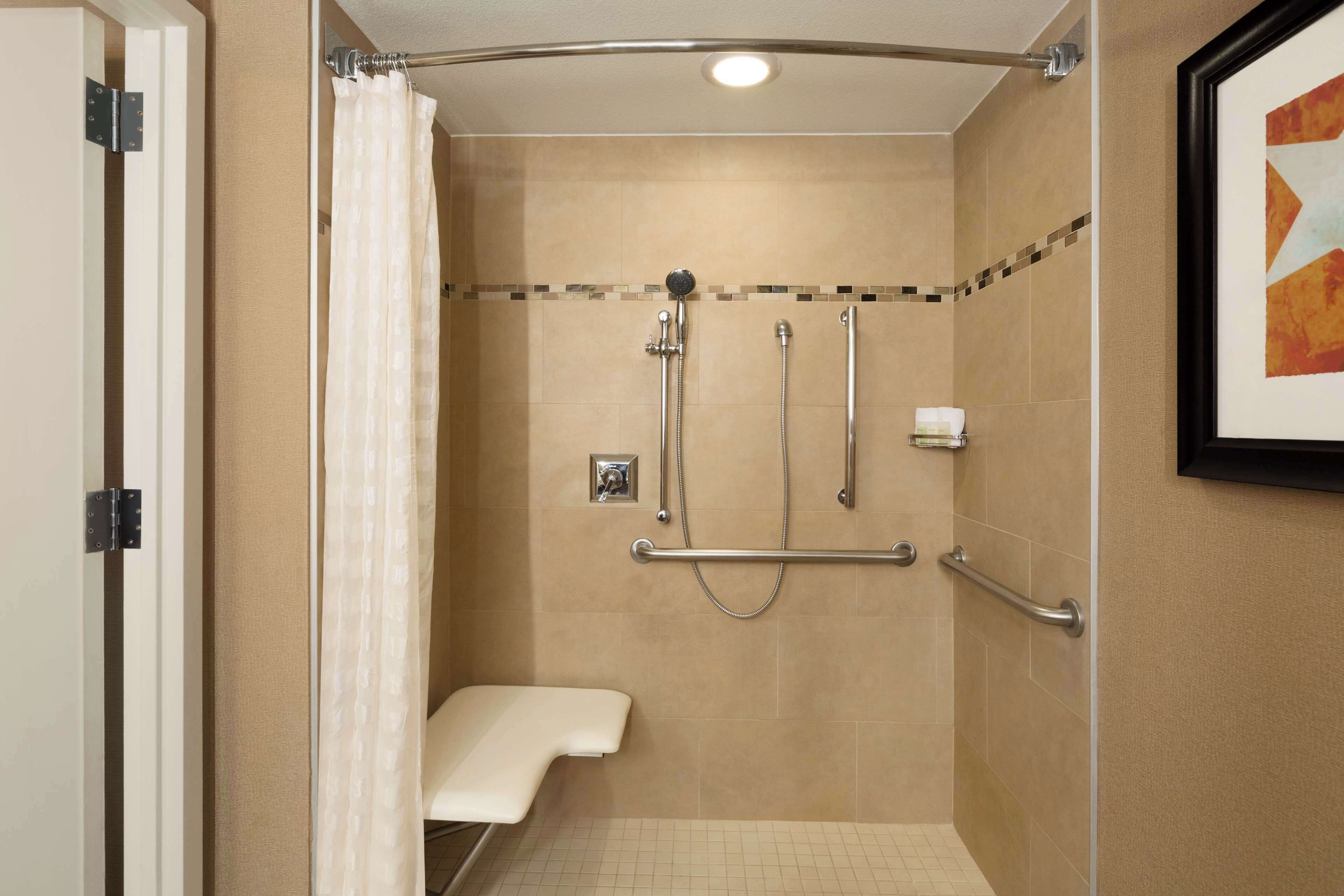 A shower with a bench, grab bars, and a tiled wall.