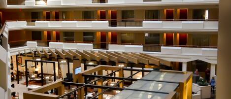 A multi-level hotel atrium with open-plan dining areas, multiple floors with balconies, and a central open space with seating.